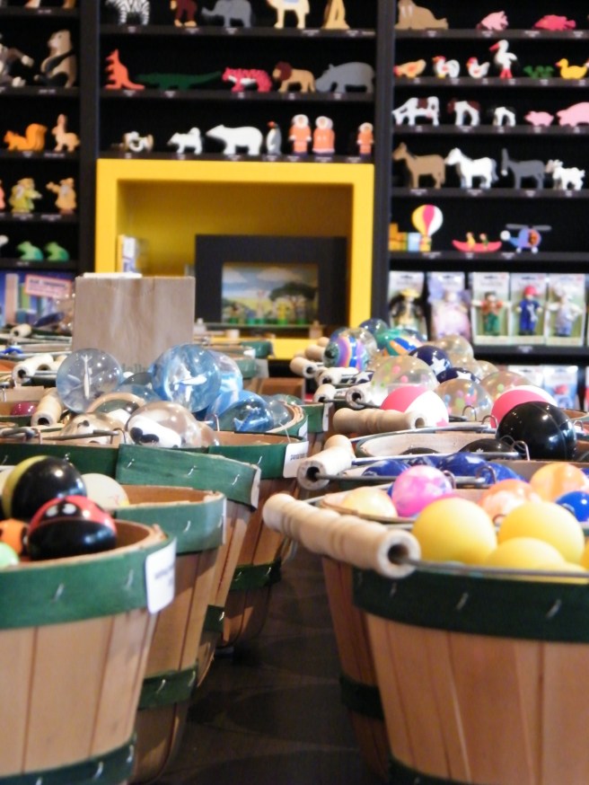 Wooden baskets with dowel handles full of small toys. In the background, a shelved wall full of wooden animal shapes. Wooden baskets with dowel handles full of small toys. In the background, a shelved wall full of wooden animal shapes.