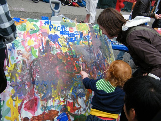 Kids collaboratively paint a picture, where cars usually are.