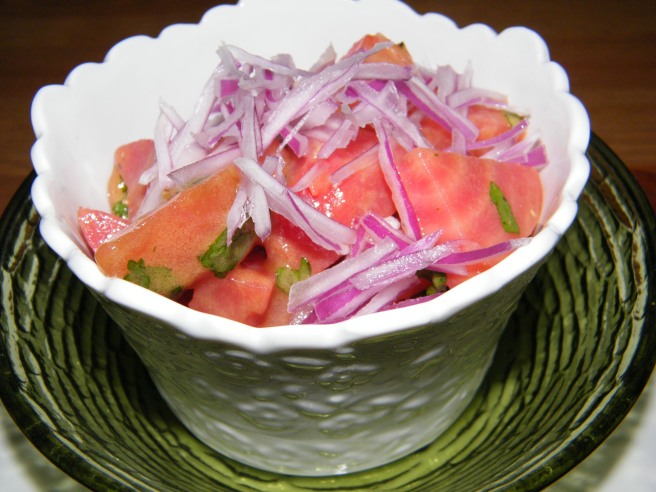 The completed salad in a fluted white bowl sitting in a green glass dish.