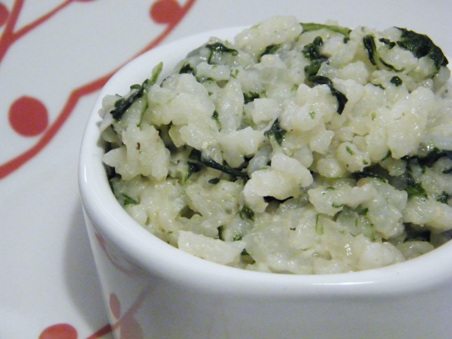 Rice, studded with pieces of spinach, in a small bowl atop a plate with red decorations,