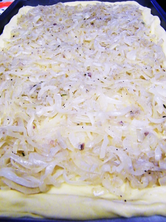 Spreading the slowly-cooked onions onto the unbaked crust.