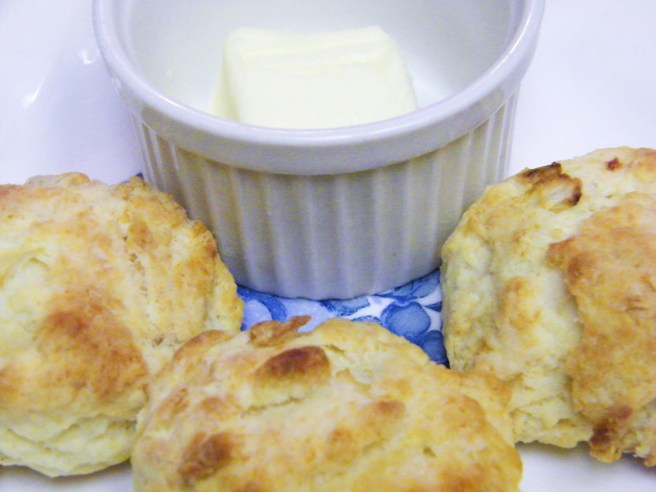 Three biscuits on a white and blue plate, with a bit of butter in a ramekin.