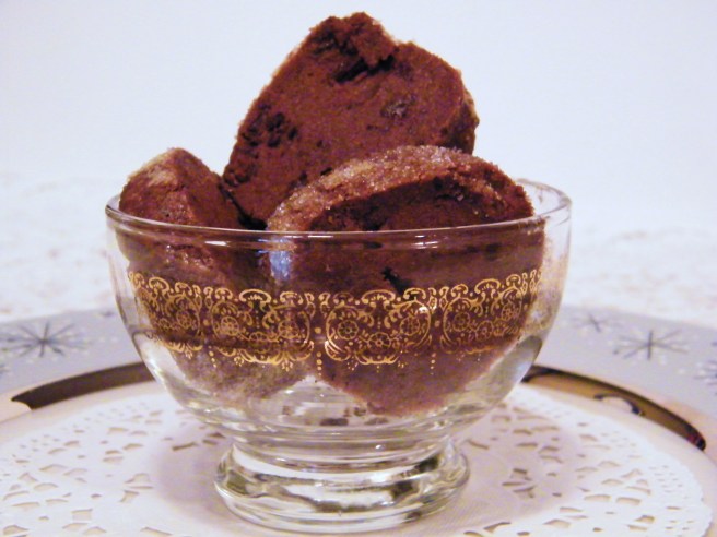 The finished cookies, in a glass dish with a gold stencil, on a doily atop a grey and silver plate.