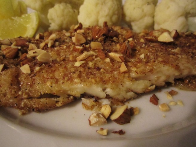 Sole, coated in an almond-lemon zest crust, with cauliflower and lemon wedges in the background.