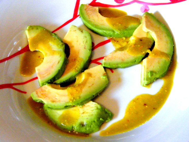 Avocado, drizzled with pistachio oil and lemon juice, atop a white and red plate.